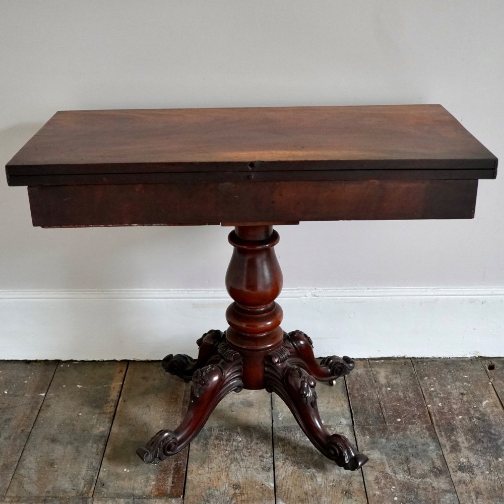 A Victorian figured mahogany card table featuring a turnover top, carved frieze, turned pedestal, and scroll legs with castors. View XII