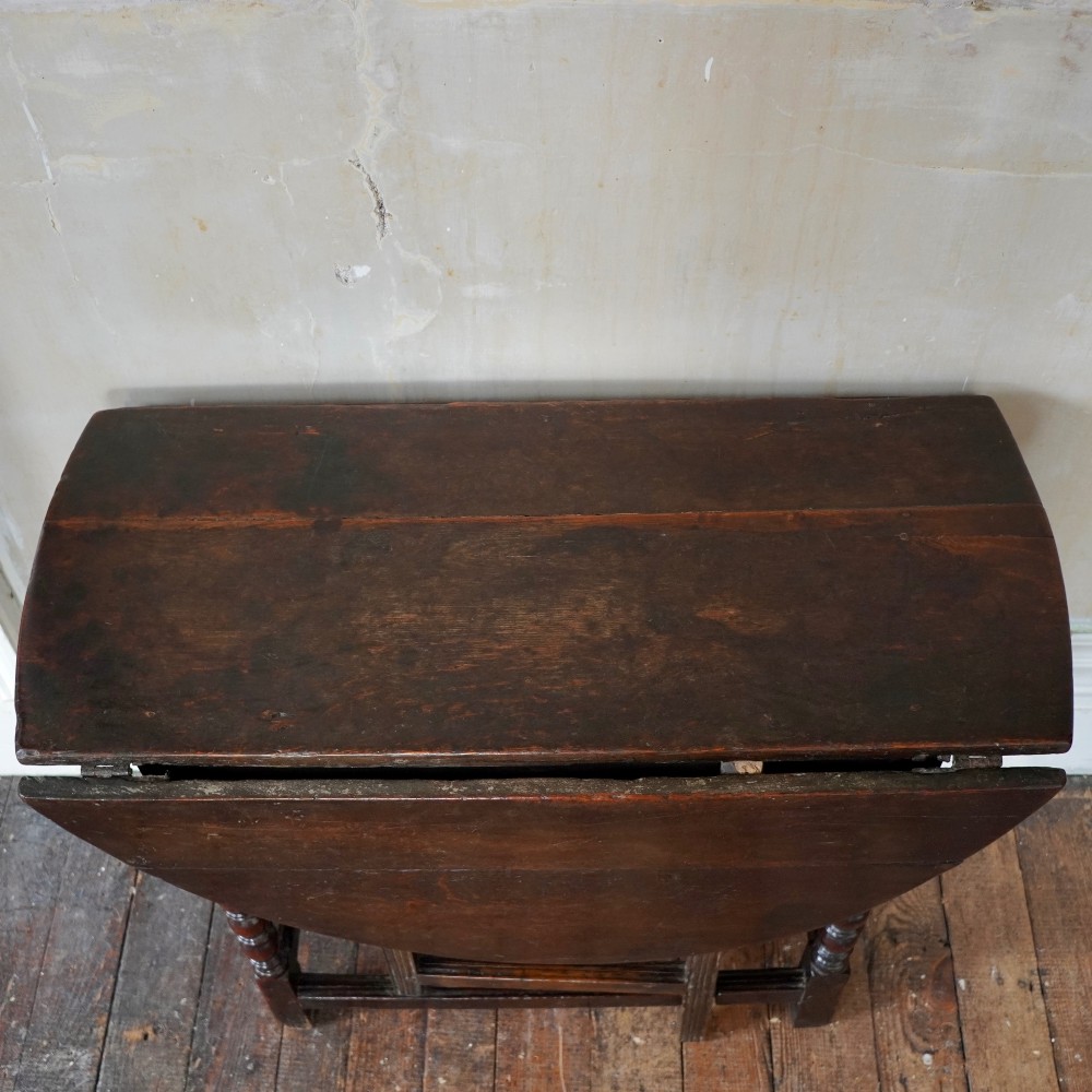 A dark brown antique oak gateleg drop-leaf table with turned legs and an oval top. View V