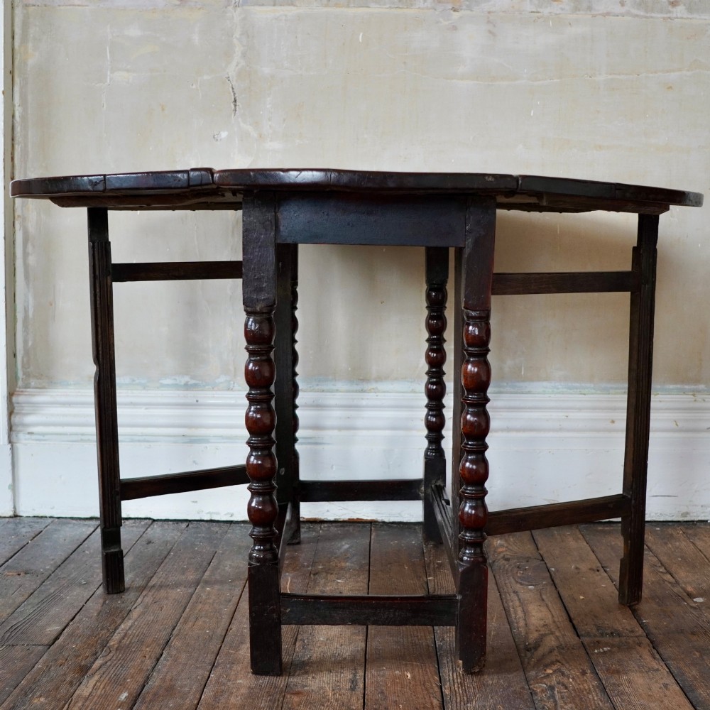 A dark brown antique oak gateleg drop-leaf table with turned legs and an oval top. View XIV