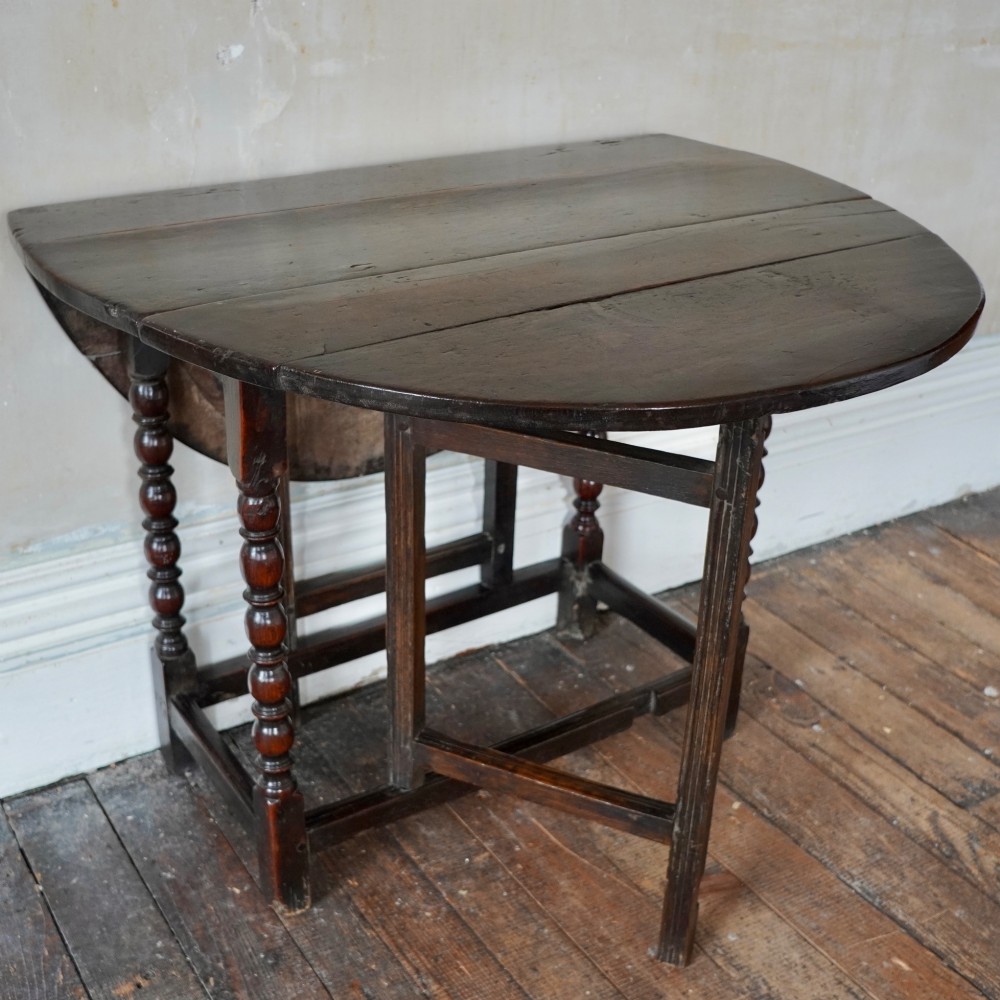 A dark brown antique oak gateleg drop-leaf table with turned legs and an oval top. View XV