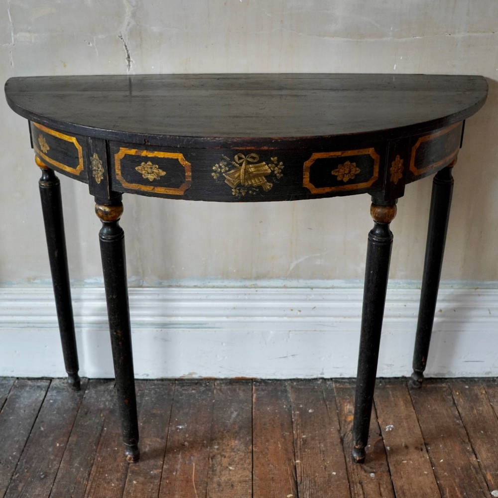 A Regency period semi-circular console table painted black with gold-gilded classical panel motifs and four slender turned legs. View III
