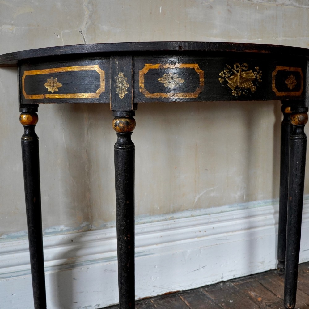 A Regency period semi-circular console table painted black with gold-gilded classical panel motifs and four slender turned legs. View V