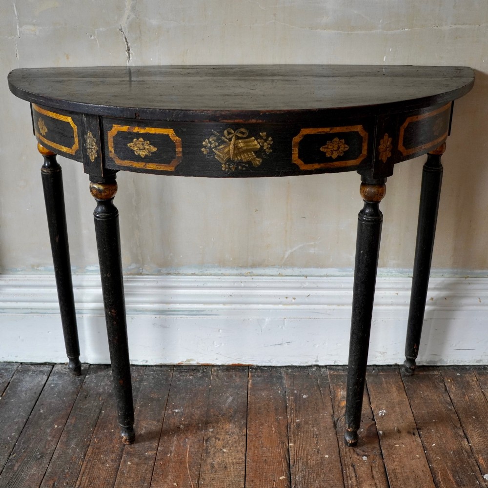 A Regency period semi-circular console table painted black with gold-gilded classical panel motifs and four slender turned legs. View VI