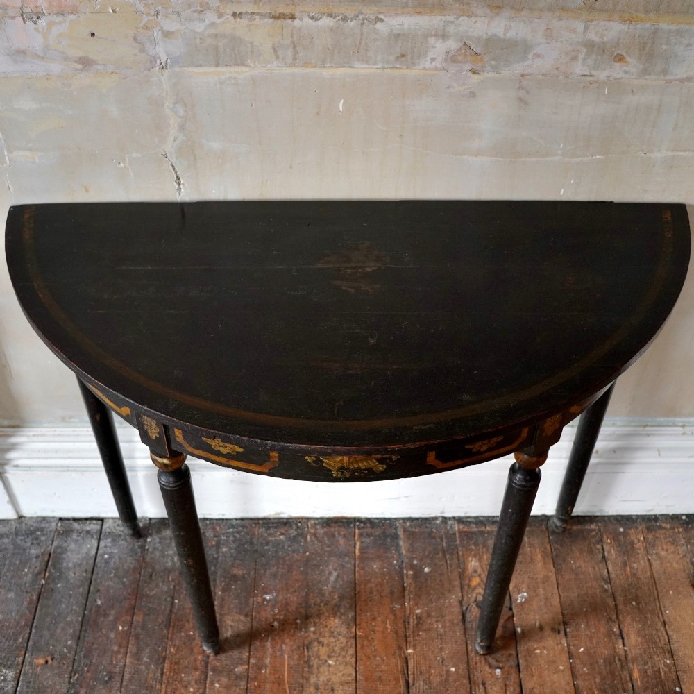 A Regency period semi-circular console table painted black with gold-gilded classical panel motifs and four slender turned legs. View VIII
