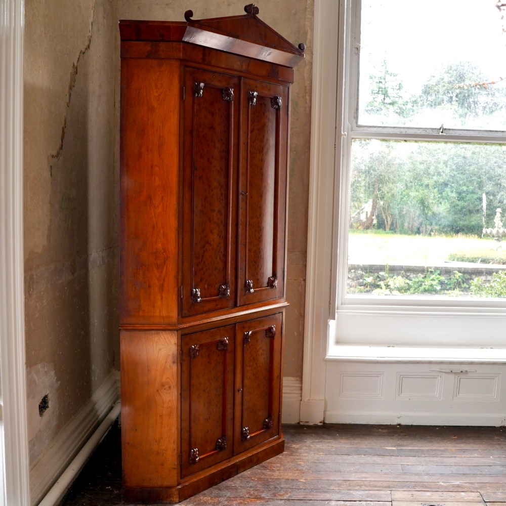 A tall, two-tier William IV corner cupboard crafted from dark plum pudding mahogany, featuring panelled double doors on both top and bottom sections with carved detail and a pediment top. View XI