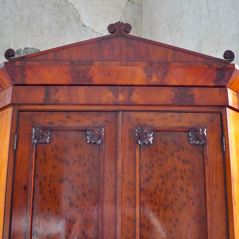 A tall, two-tier William IV corner cupboard crafted from dark plum pudding mahogany, featuring panelled double doors on both top and bottom sections with carved detail and a pediment top. View XII