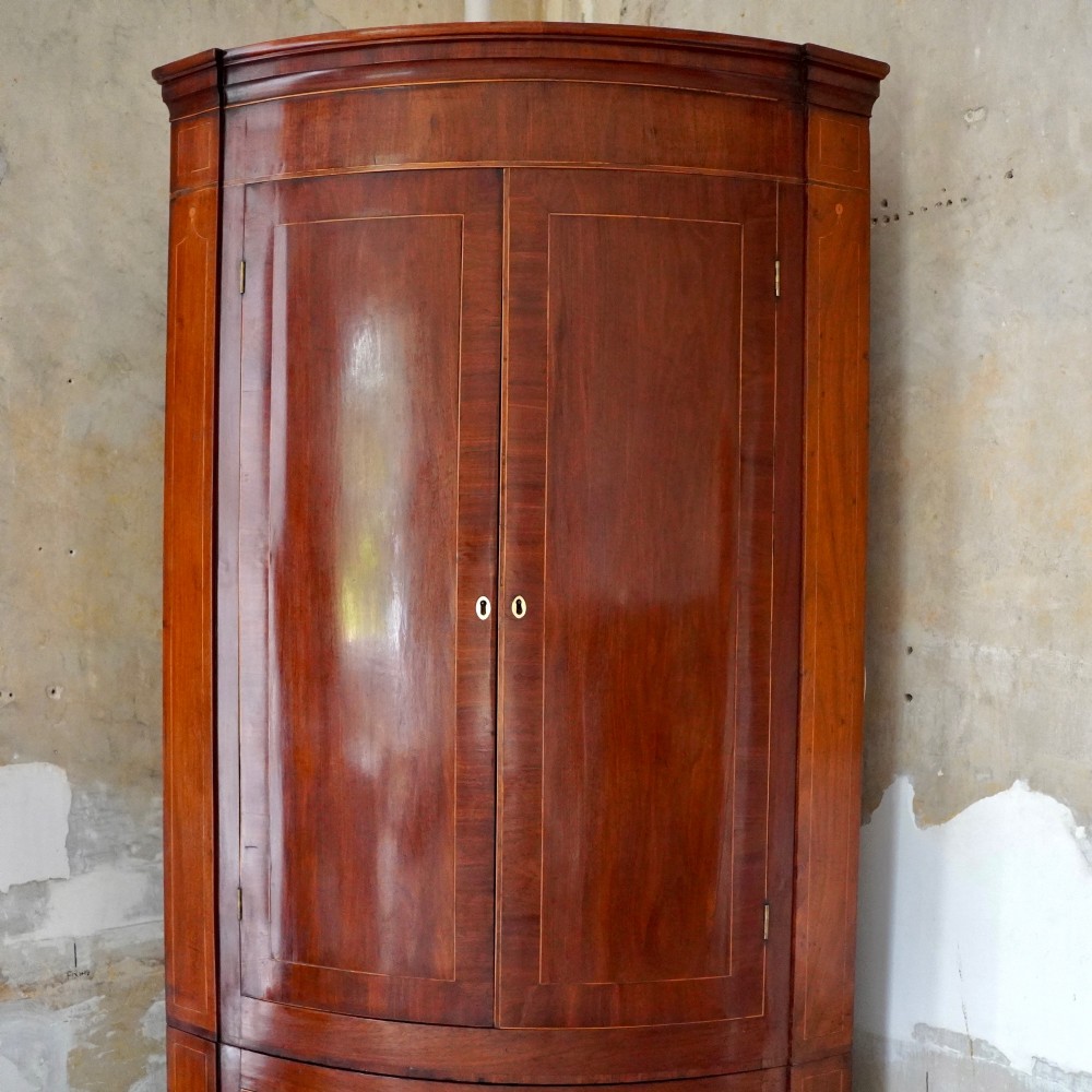 A tall Georgian mahogany bowfront corner cupboard featuring two upper curved doors, two lower curved doors, and fine line inlay. View II