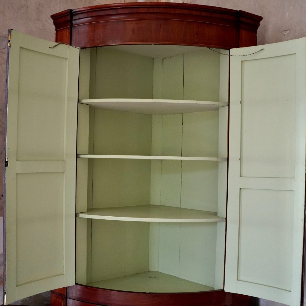 A tall Georgian mahogany bowfront corner cupboard featuring two upper curved doors, two lower curved doors, and fine line inlay. View IV