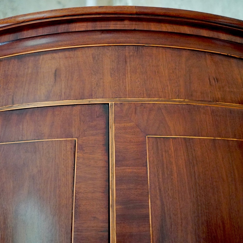 A tall Georgian mahogany bowfront corner cupboard featuring two upper curved doors, two lower curved doors, and fine line inlay. View VII