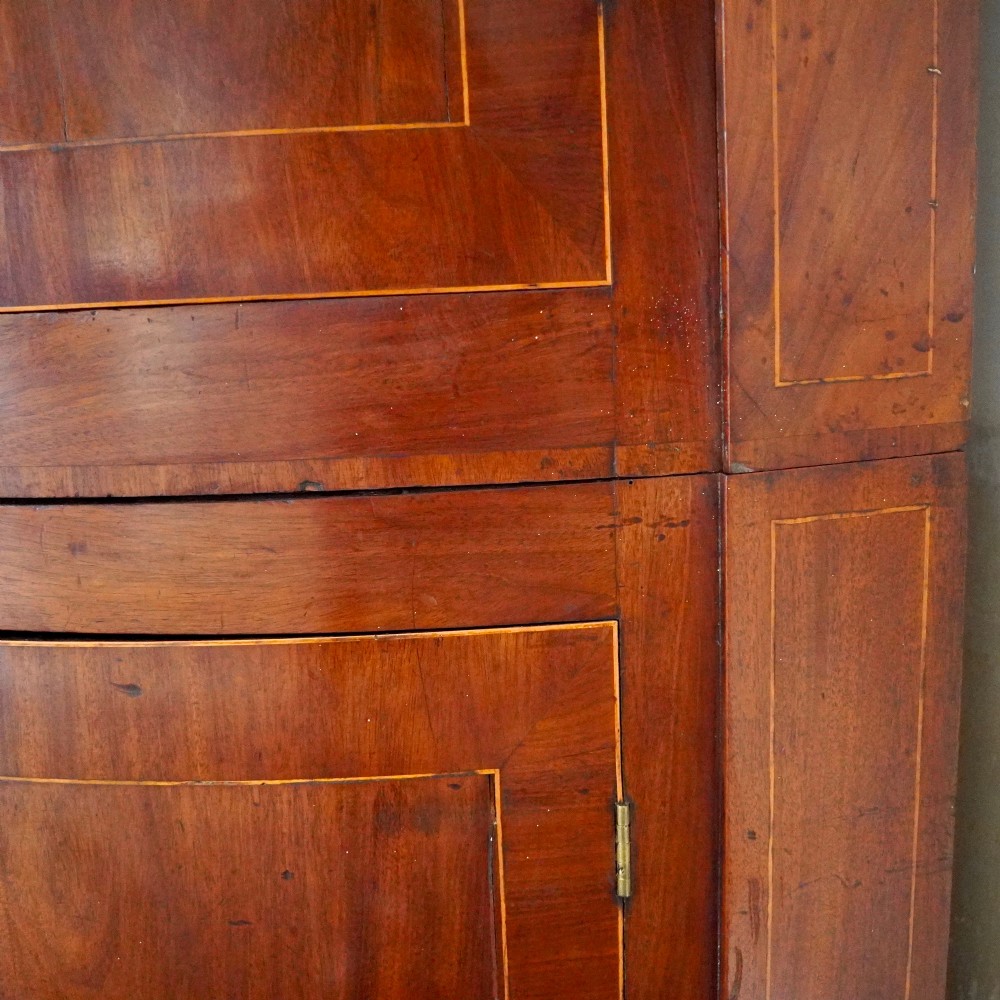 A tall Georgian mahogany bowfront corner cupboard featuring two upper curved doors, two lower curved doors, and fine line inlay. View IX