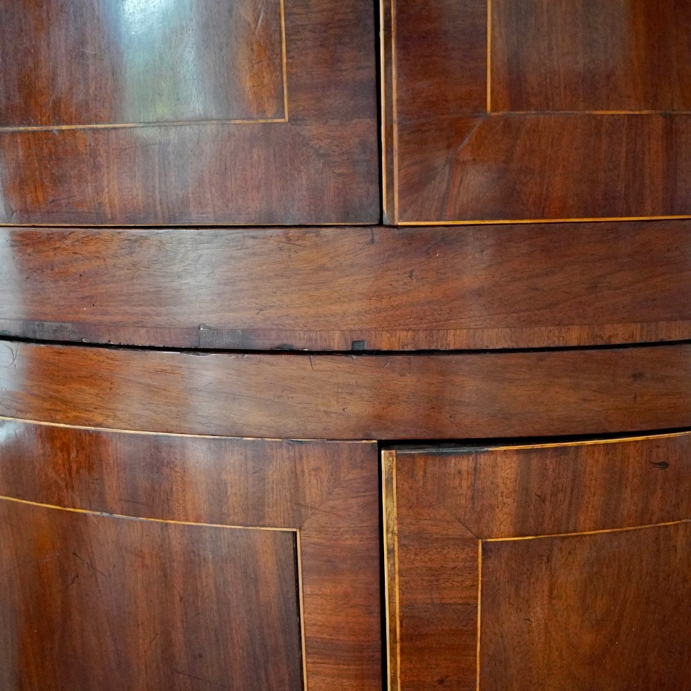 A tall Georgian mahogany bowfront corner cupboard featuring two upper curved doors, two lower curved doors, and fine line inlay. View X