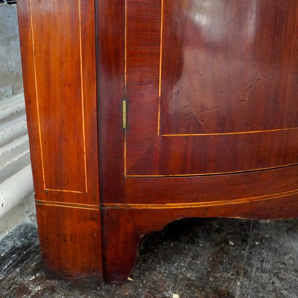 A tall Georgian mahogany bowfront corner cupboard featuring two upper curved doors, two lower curved doors, and fine line inlay. View XII