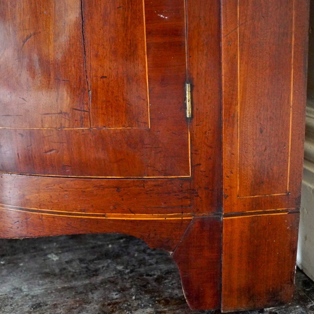 A tall Georgian mahogany bowfront corner cupboard featuring two upper curved doors, two lower curved doors, and fine line inlay. View XIV