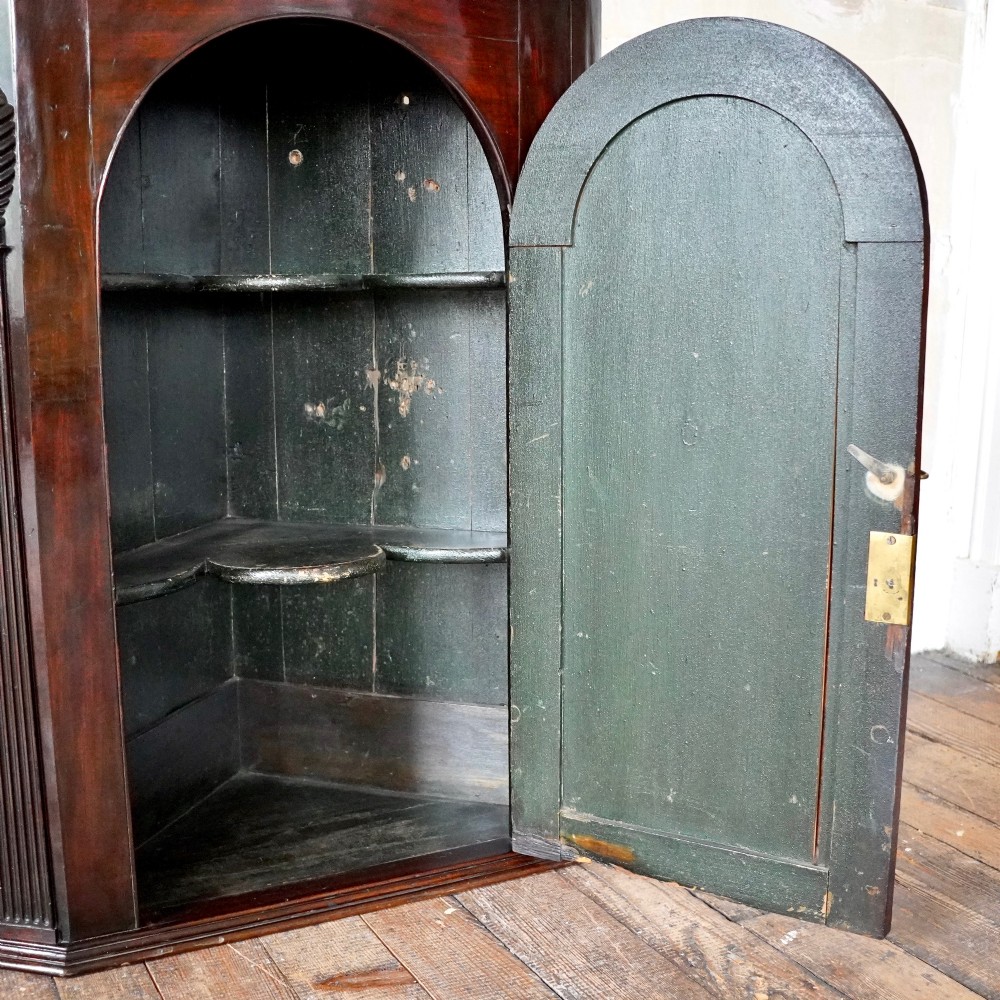 Mid-18th century Georgian mahogany hanging corner cupboard featuring an arched panelled door, brass hardware, and fluted pilasters. View IV