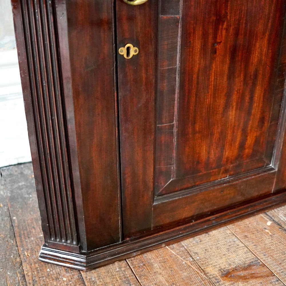 Mid-18th century Georgian mahogany hanging corner cupboard featuring an arched panelled door, brass hardware, and fluted pilasters. View VI