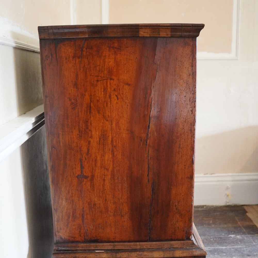 An early eighteenth-century Queen Anne walnut chest on stand featuring multiple drawers, brass teardrop handles, a shaped apron, and turned legs connected by stretchers. View XIII
