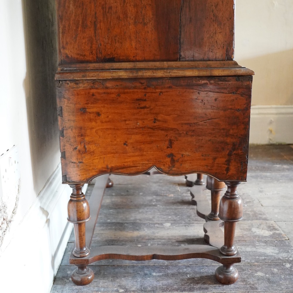 An early eighteenth-century Queen Anne walnut chest on stand featuring multiple drawers, brass teardrop handles, a shaped apron, and turned legs connected by stretchers. View XIV