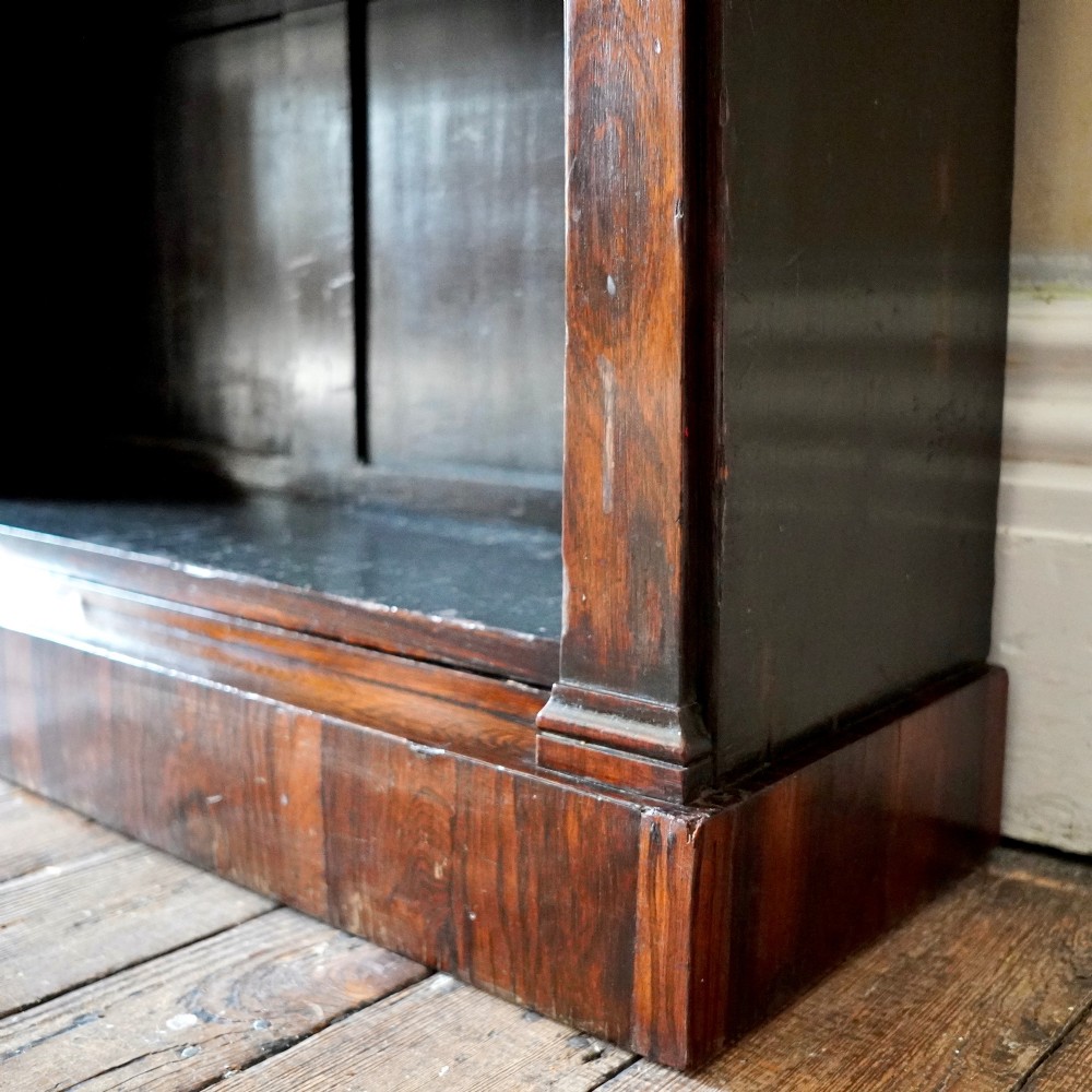 An antique William IV rosewood open bookcase featuring two adjustable shelves, a solid plinth base, and carved scroll capitals atop side pilasters. View X
