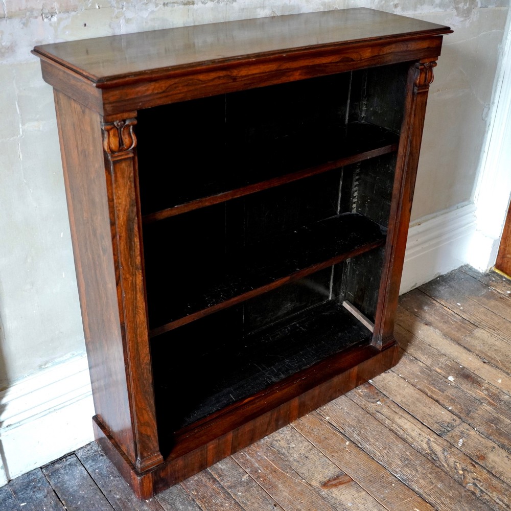 An antique William IV rosewood open bookcase featuring two adjustable shelves, a solid plinth base, and carved scroll capitals atop side pilasters. View XI