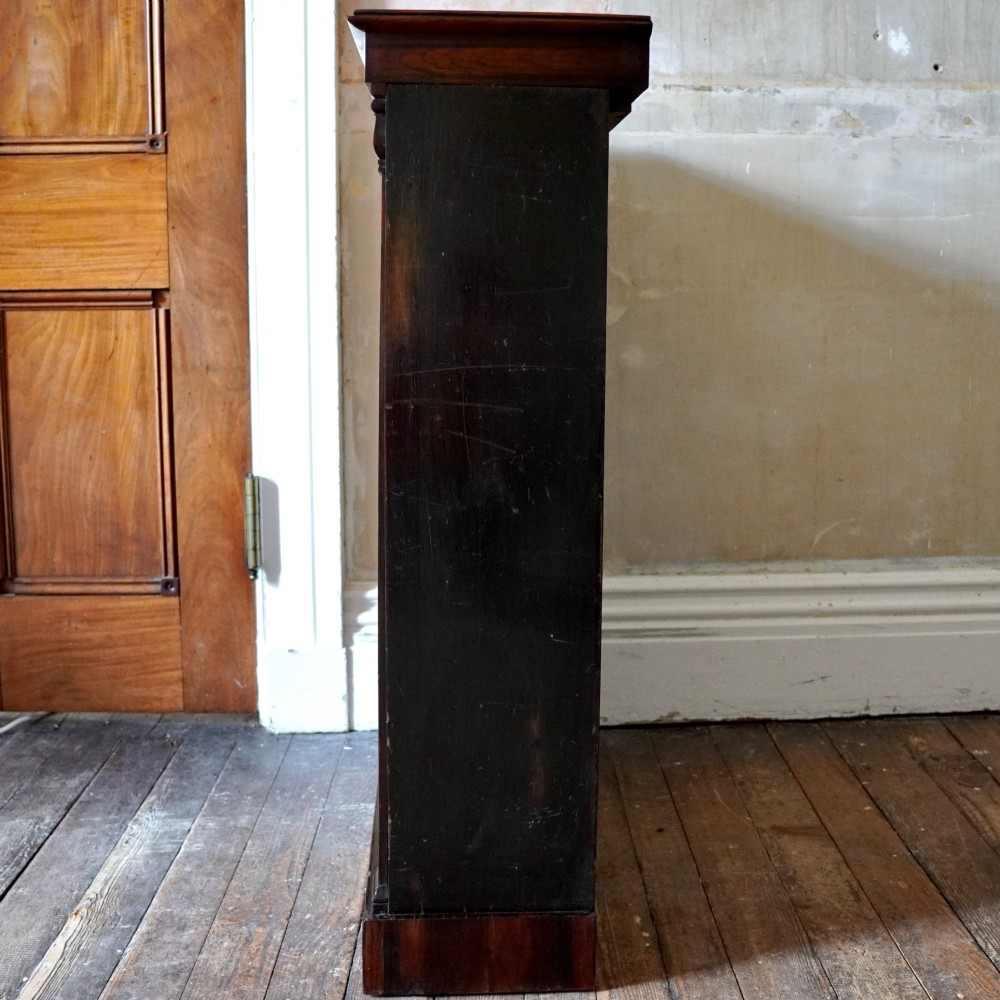 An antique William IV rosewood open bookcase featuring two adjustable shelves, a solid plinth base, and carved scroll capitals atop side pilasters. View XII