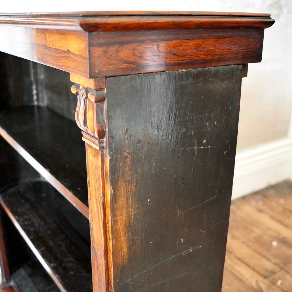 An antique William IV rosewood open bookcase featuring two adjustable shelves, a solid plinth base, and carved scroll capitals atop side pilasters. View XIII