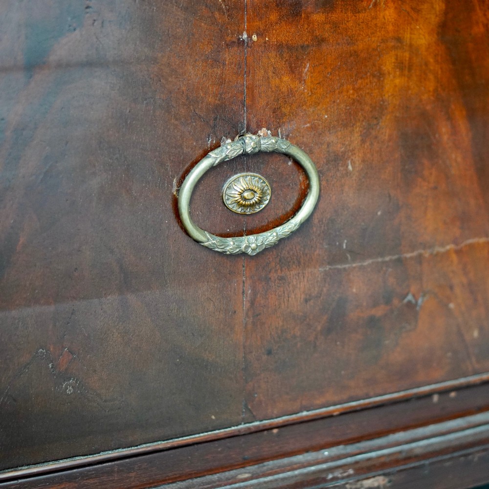 A George III bowfront mahogany wardrobe featuring twin panelled doors with oval flame mahogany veneers above two drawers and flared bracket feet. View VI