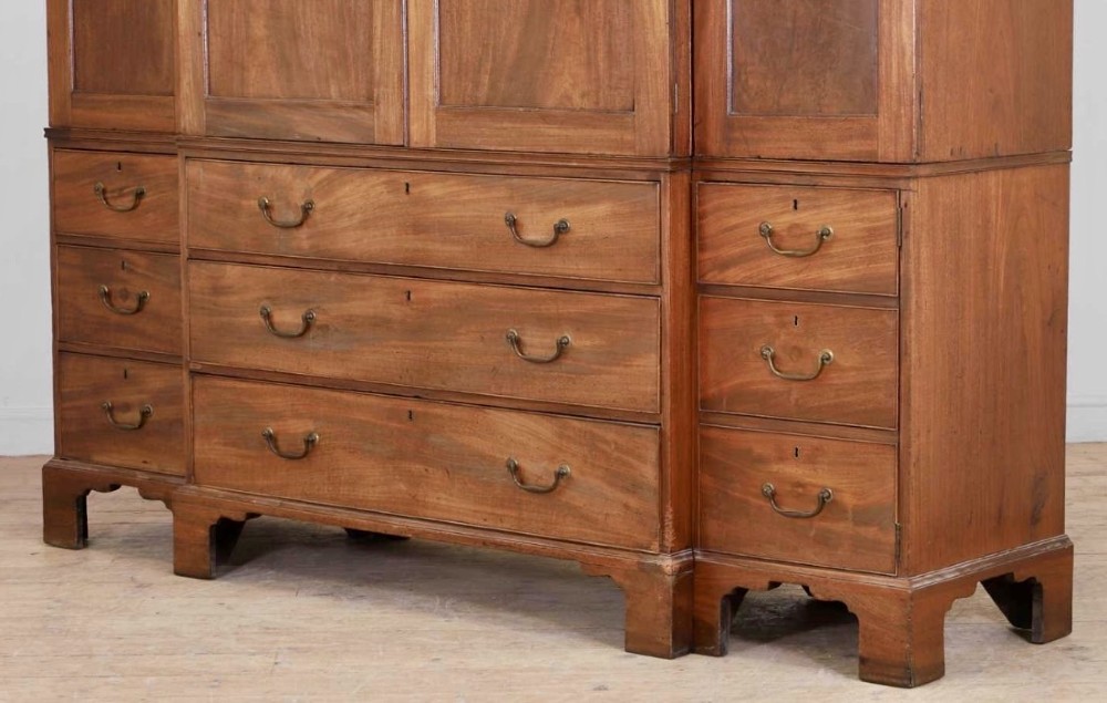 A large George III mahogany breakfront linen press wardrobe featuring central panelled doors above drawers, flanked by side cupboards on bracket feet. View V