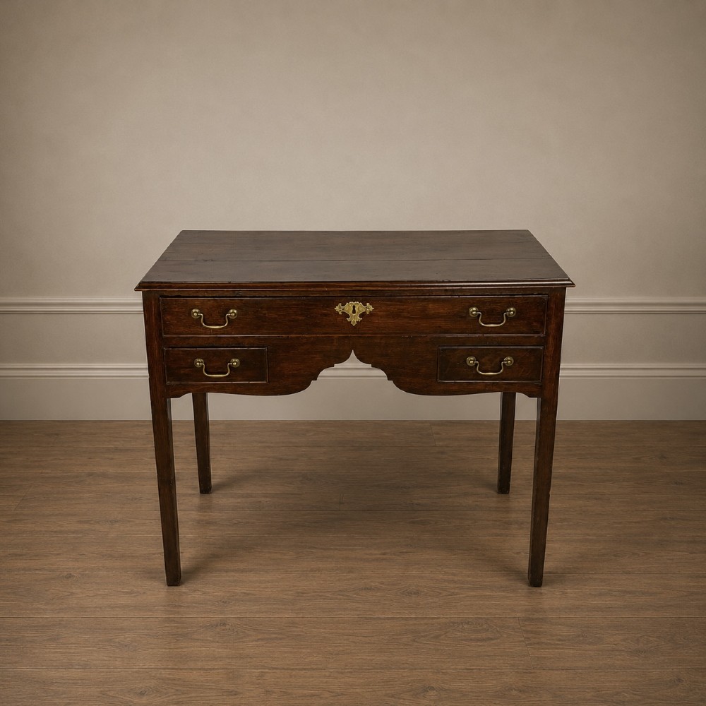 A George III dark oak lowboy table featuring three drawers with brass swan-neck handles, a shaped apron, and four square straight legs.