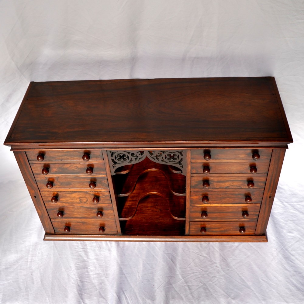 A Regency period dark rosewood tabletop collectors cabinet featuring twin banks of small drawers flanking a central mirrored shelf unit with Gothic arched carving. View IV