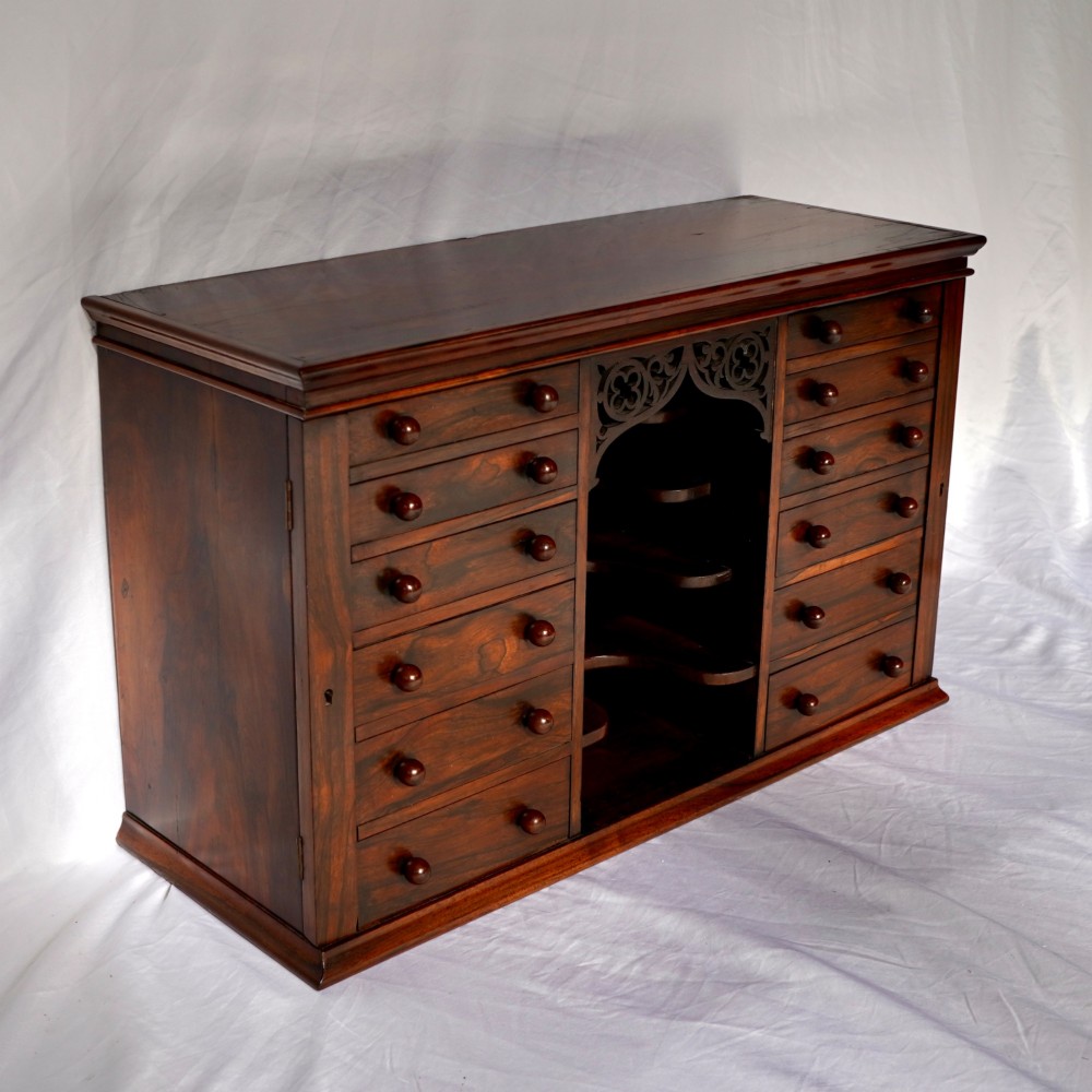 A Regency period dark rosewood tabletop collectors cabinet featuring twin banks of small drawers flanking a central mirrored shelf unit with Gothic arched carving. View VII