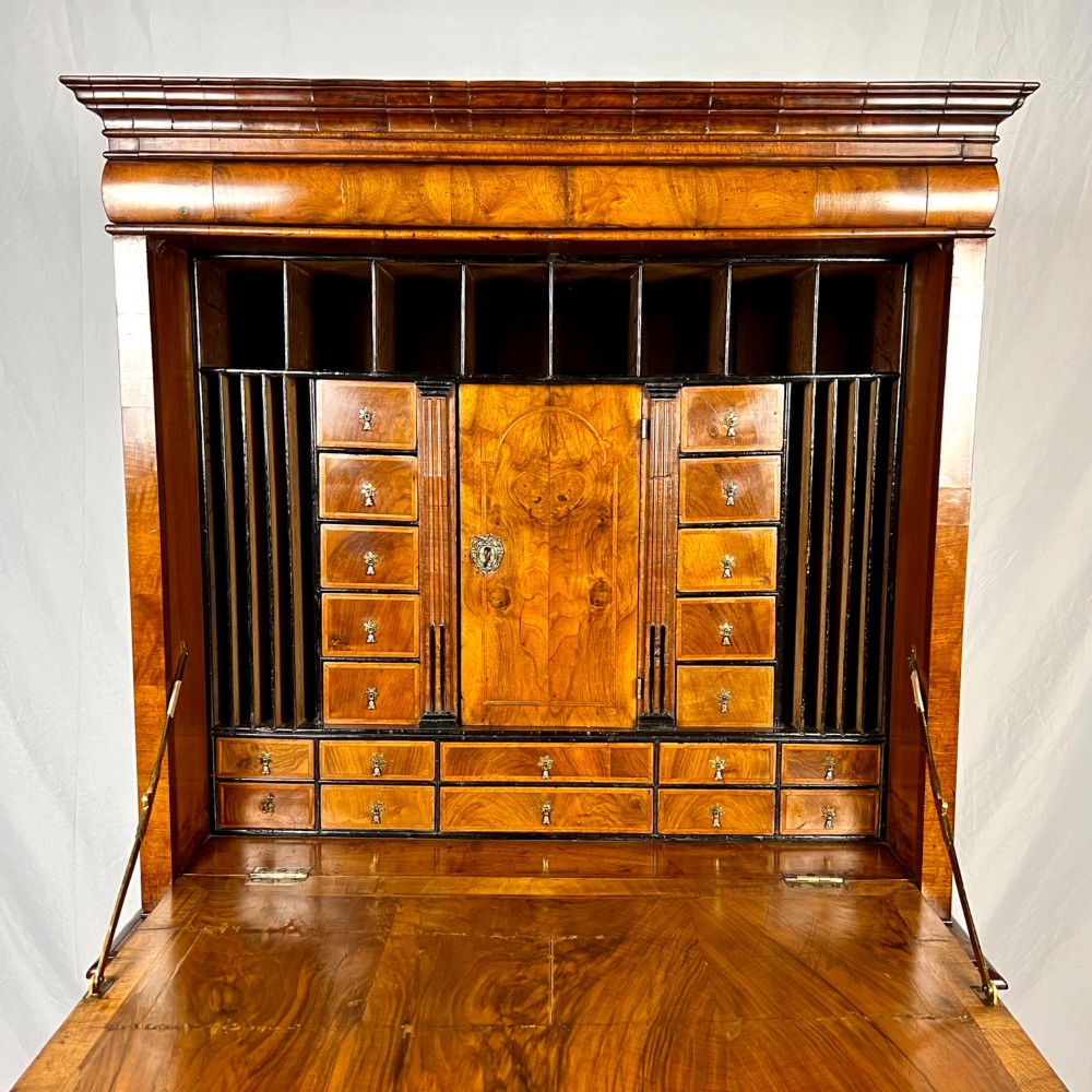 An eighteenth-century early Georgian figured walnut escritoire featuring an open fall-front revealing a detailed fitted interior above a lower chest of drawers with brass handles. View II