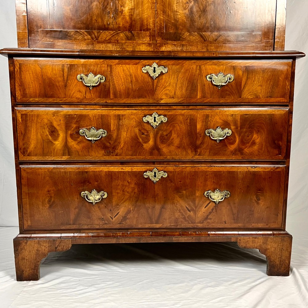 An eighteenth-century early Georgian figured walnut escritoire featuring an open fall-front revealing a detailed fitted interior above a lower chest of drawers with brass handles. View VI