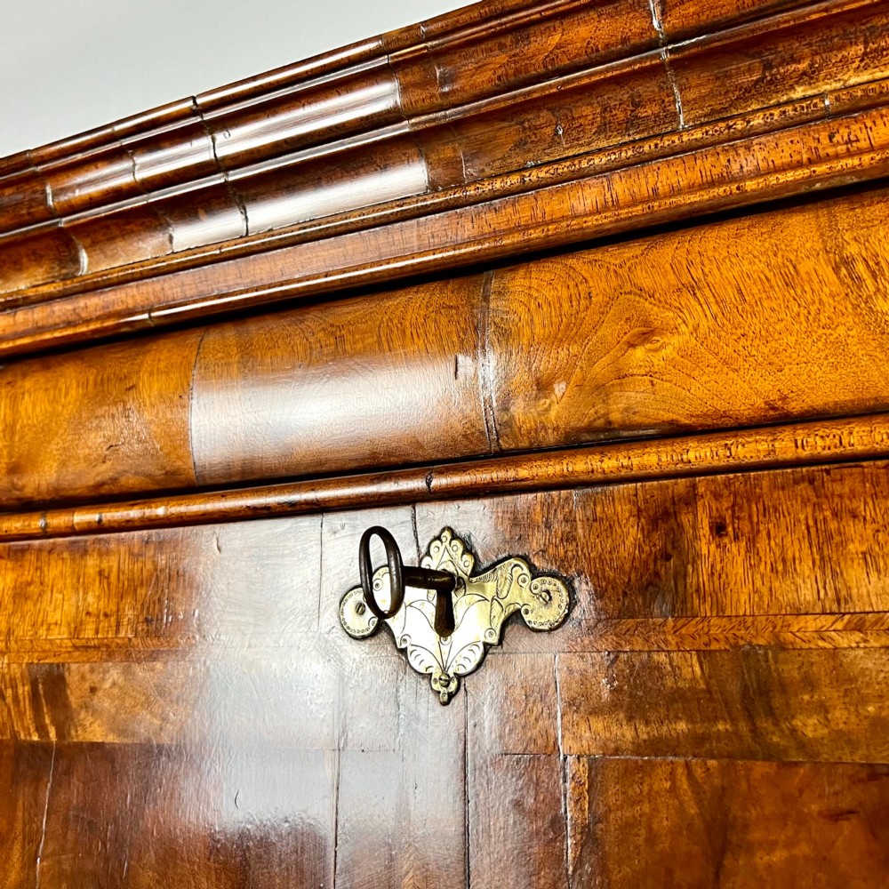An eighteenth-century early Georgian figured walnut escritoire featuring an open fall-front revealing a detailed fitted interior above a lower chest of drawers with brass handles. View VIII