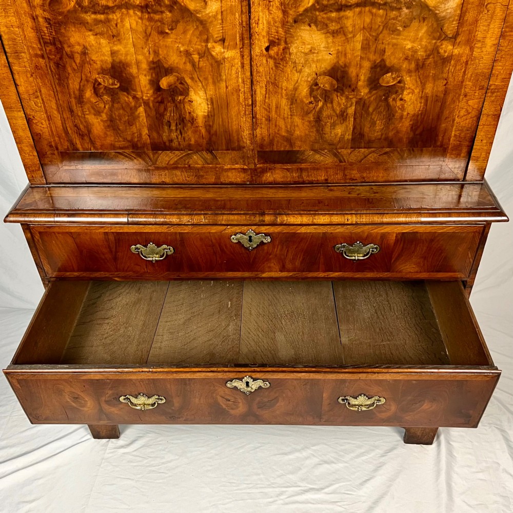 An eighteenth-century early Georgian figured walnut escritoire featuring an open fall-front revealing a detailed fitted interior above a lower chest of drawers with brass handles. View IX