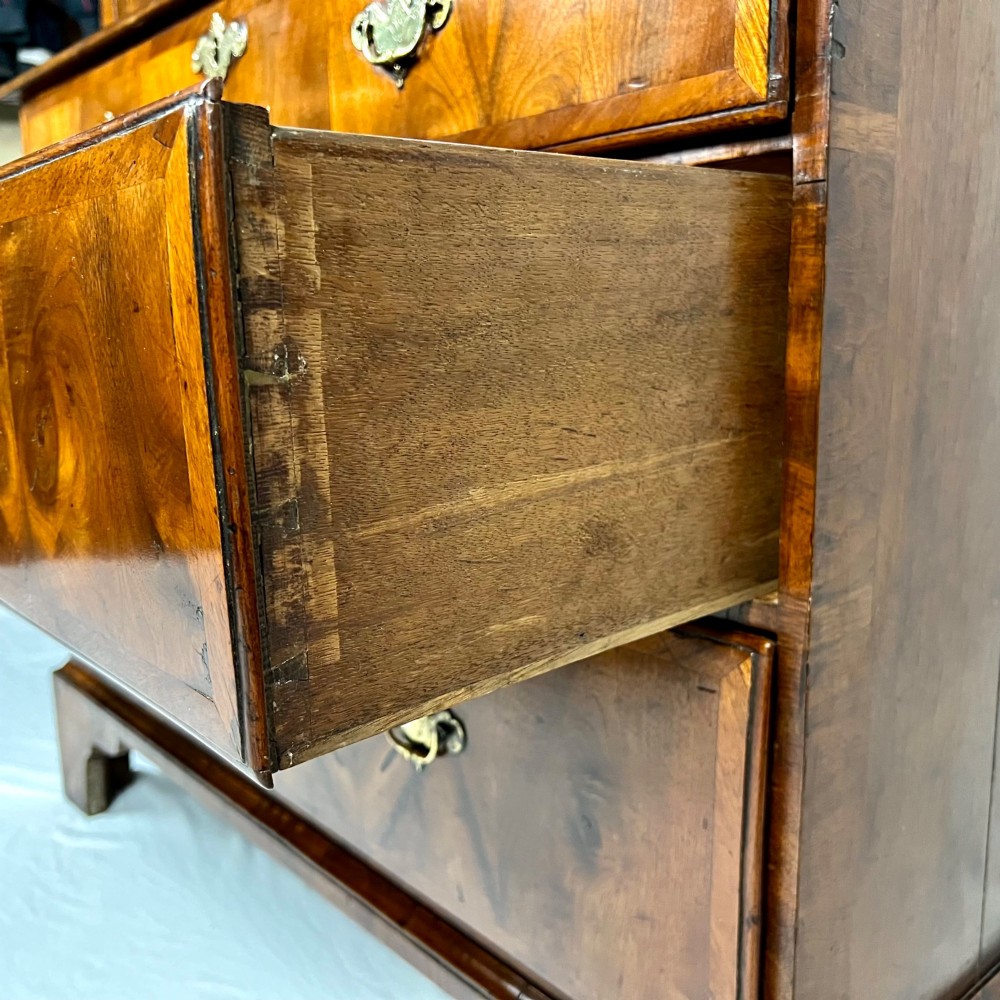 An eighteenth-century early Georgian figured walnut escritoire featuring an open fall-front revealing a detailed fitted interior above a lower chest of drawers with brass handles. View X