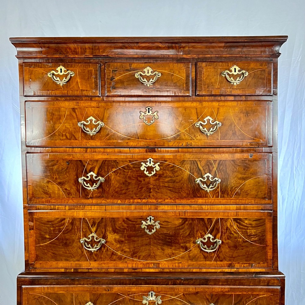 A tall George II two-part walnut chest on chest featuring figured burr walnut drawer fronts with line inlay, brass swan-neck handles, and bracket feet. View II