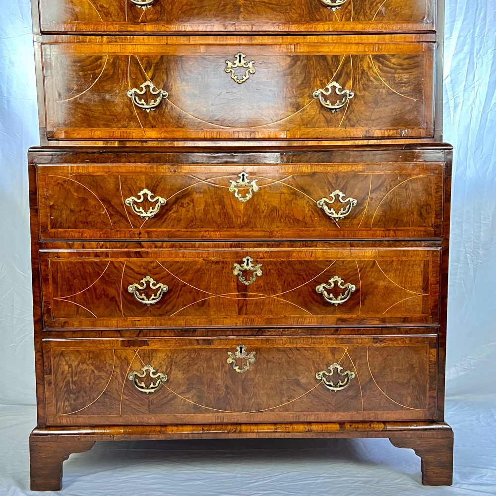 A tall George II two-part walnut chest on chest featuring figured burr walnut drawer fronts with line inlay, brass swan-neck handles, and bracket feet. View III