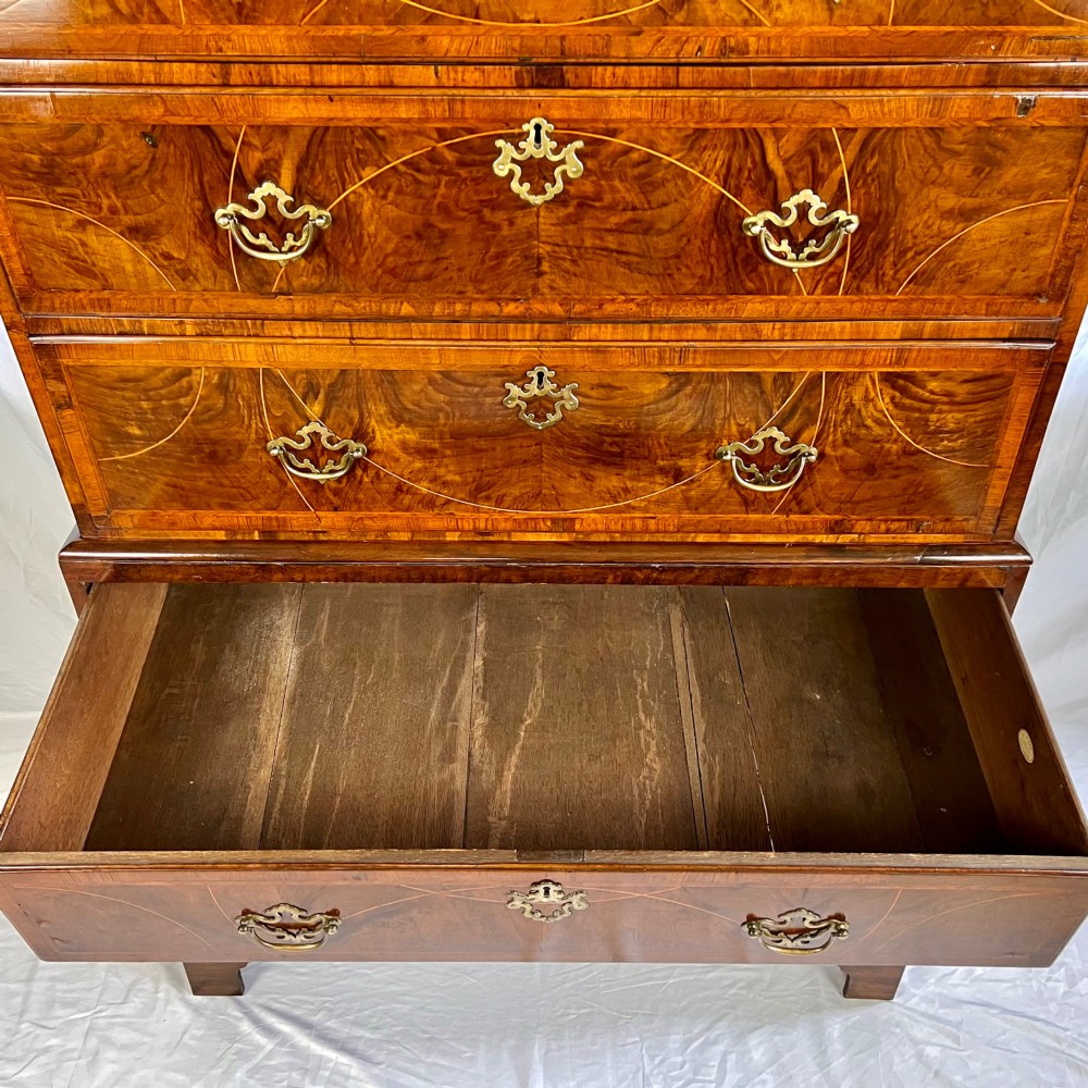 A tall George II two-part walnut chest on chest featuring figured burr walnut drawer fronts with line inlay, brass swan-neck handles, and bracket feet. View IV