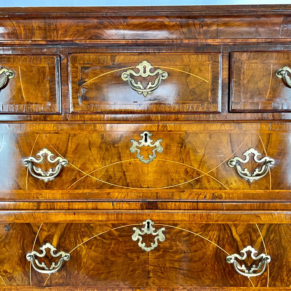 A tall George II two-part walnut chest on chest featuring figured burr walnut drawer fronts with line inlay, brass swan-neck handles, and bracket feet. View X