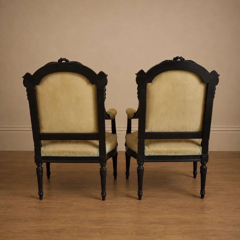 A pair of ebonised beech Louis XVI Revival salon armchairs featuring carved frames, fluted legs, padded armrests, and tapestry upholstery, accompanied by matching footstools. View XIV