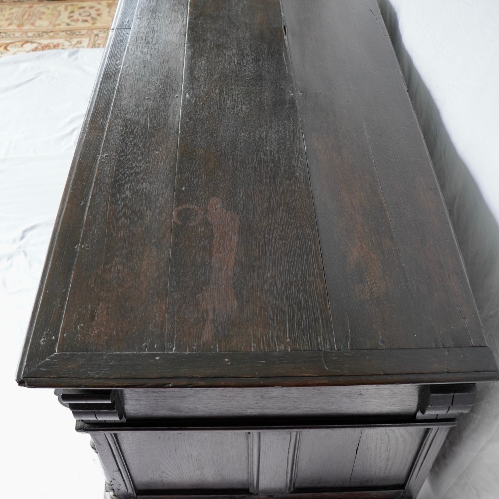 A dark oak 17th-century style chest of drawers featuring geometric timber inlay along the top frieze, applied mouldings, and brass drop handles. View XII