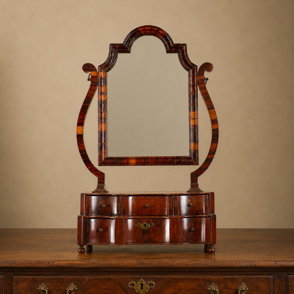 An antique Queen Anne walnut and laburnum toilet mirror featuring an arched cross-banded frame above a serpentine base with miniature drawers.