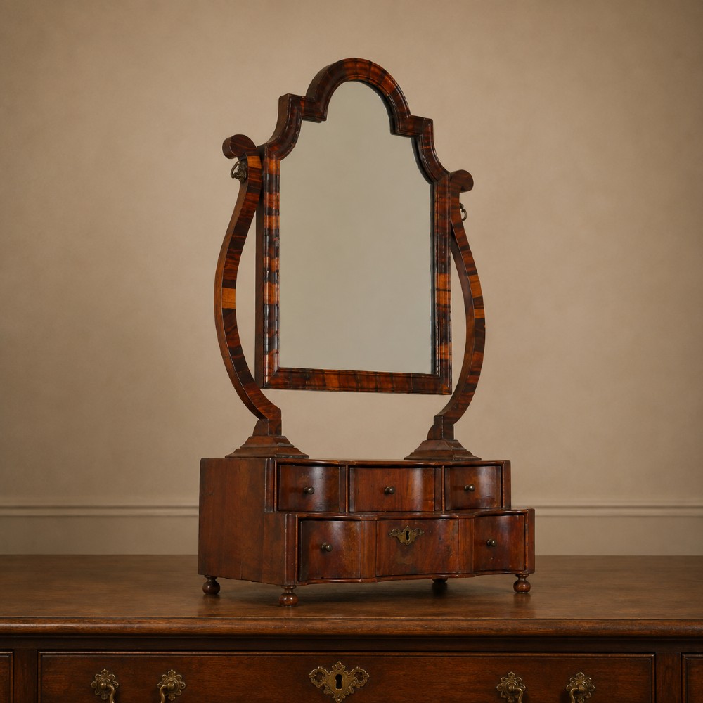 An antique Queen Anne walnut and laburnum toilet mirror featuring an arched cross-banded frame above a serpentine base with miniature drawers. View II