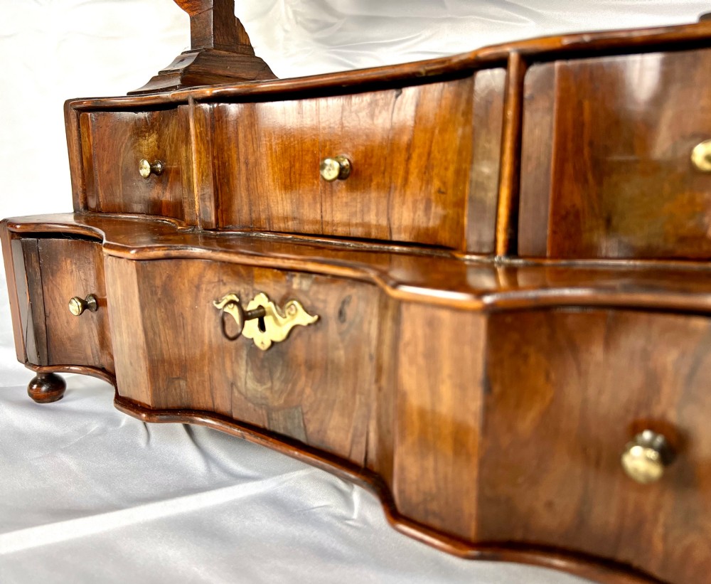 An antique Queen Anne walnut and laburnum toilet mirror featuring an arched cross-banded frame above a serpentine base with miniature drawers. View IV