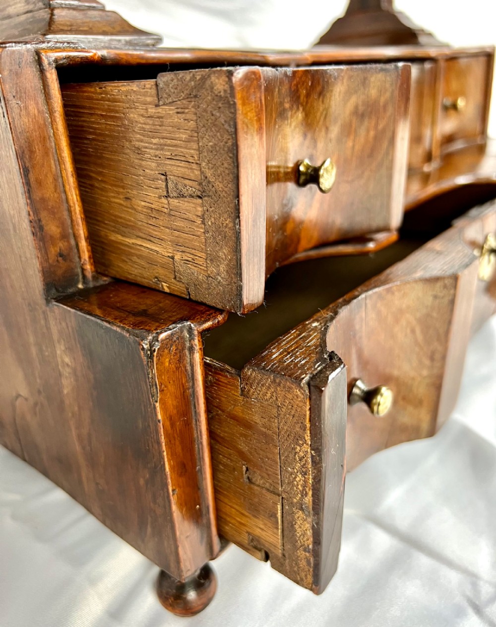 An antique Queen Anne walnut and laburnum toilet mirror featuring an arched cross-banded frame above a serpentine base with miniature drawers. View XV
