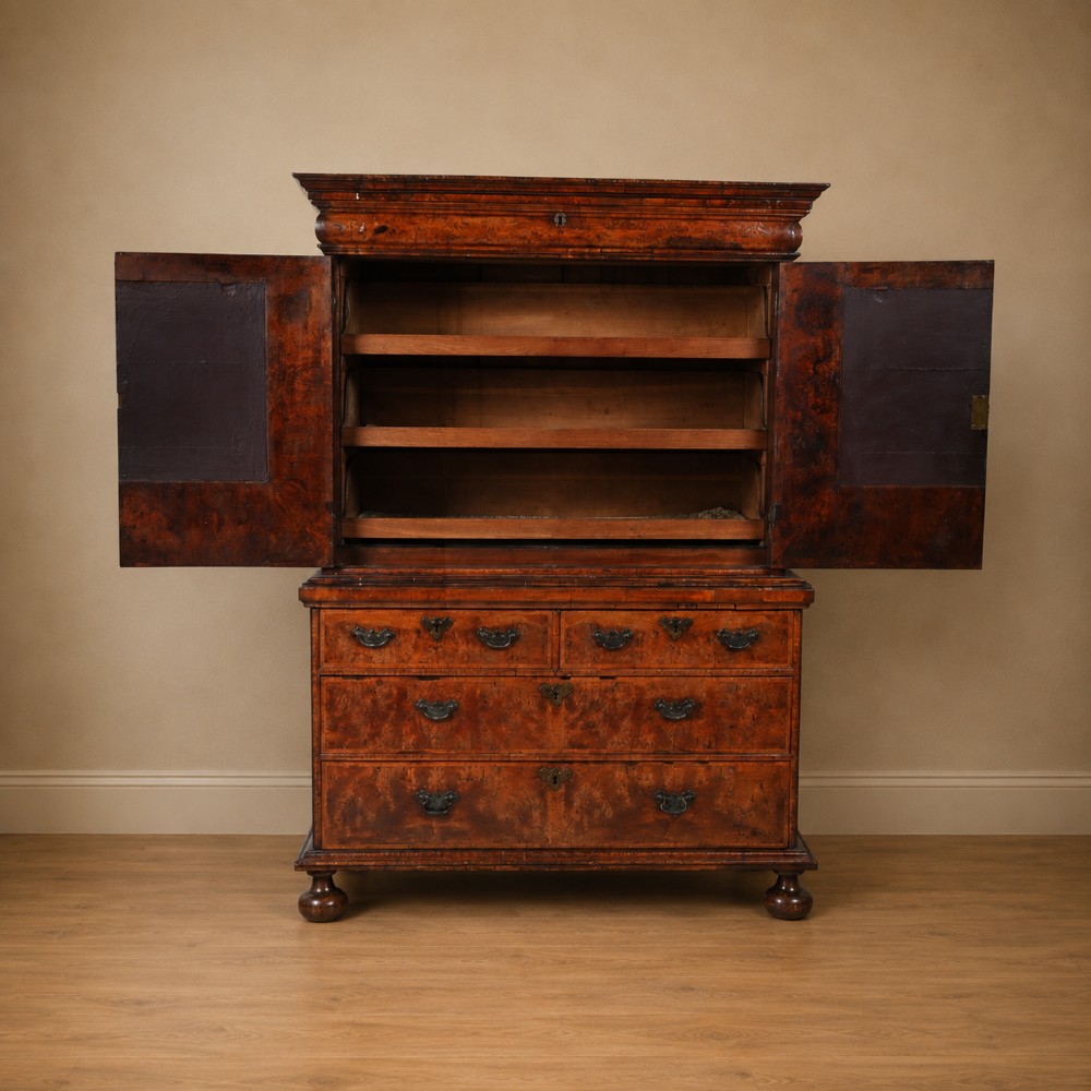 An antique Queen Anne burr walnut linen press featuring upper double cupboard doors over three lower drawers with brass handles on turned bun feet. View XII