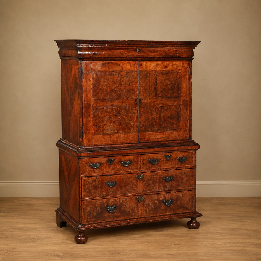 An antique Queen Anne burr walnut linen press featuring upper double cupboard doors over three lower drawers with brass handles on turned bun feet. View XIII