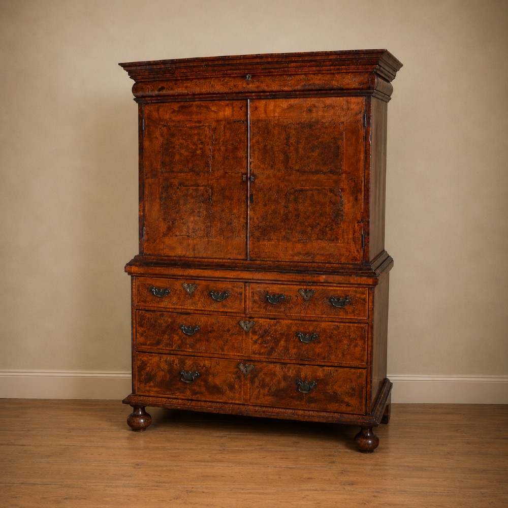 An antique Queen Anne burr walnut linen press featuring upper double cupboard doors over three lower drawers with brass handles on turned bun feet. View XIV
