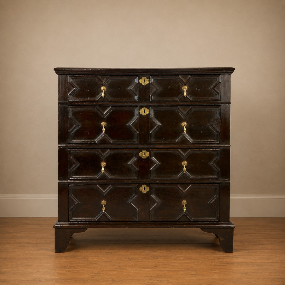 A dark oak Charles II chest of drawers featuring four geometric moulded drawer fronts with brass teardrop handles and decorative brass escutcheons.