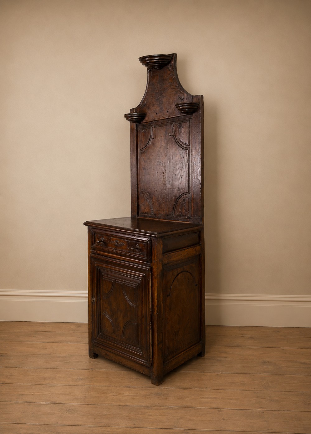 An 18th-century dark chestnut wood lavabo cabinet featuring a carved backboard mounted with a pewter cistern above a matching pewter basin. View XIV